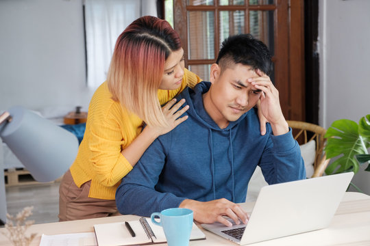 Asian female girlfriend encouragement boyfriend from stress while working on home budget on laptop at living room in home.