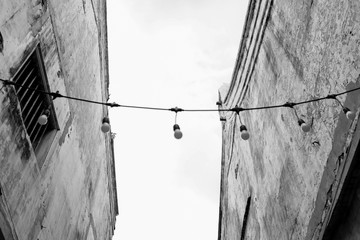 Look up side of chinese house with white weathered wall and wire string of light bulbs in black and white