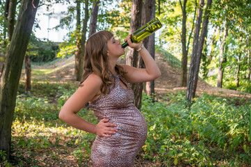Pregnant woman drinking wine in the park - alcoholism concept