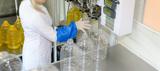 line of production of refined sunflower oil. Girl worker at a factory on a conveyor background with bottles of vegetable oil.