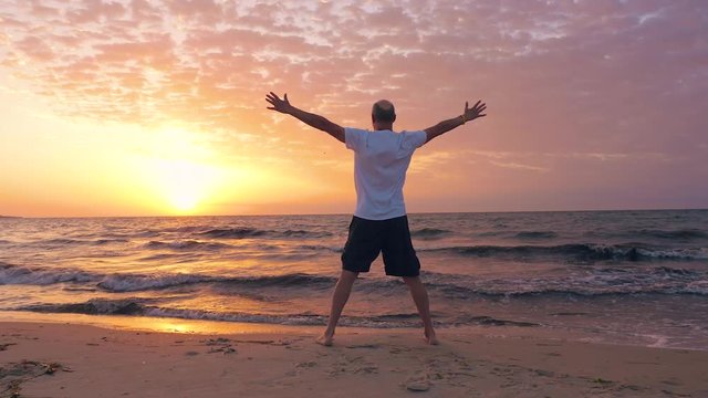 Middle aged man went up and greet sun on seashore with beautiful sunrise