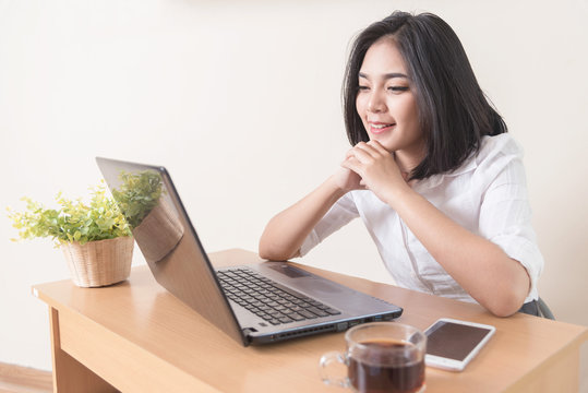 Portrait of happy successful Caucasian businesswoman in white shirt looking and smiling at the laptop camera. Attractive female manager sitting at desk after hard working day.