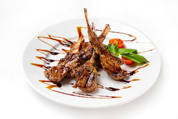 Plate of roasted lamb chops served with vegetables and sauce isolated at white background.