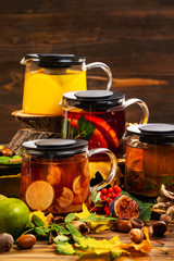 Vertical iimage of teapots set with different colorful natural tea decorated with autumn leaves at wooden dark board background.