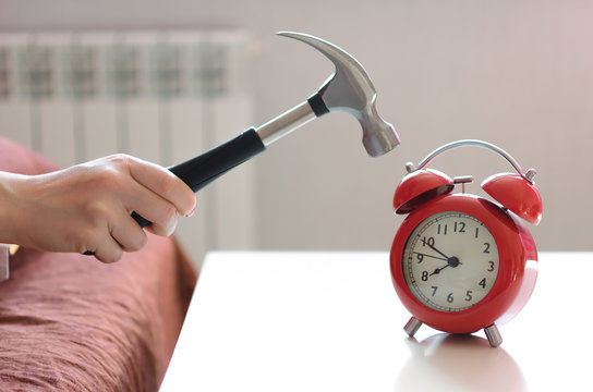 Sleepy woman in the bed is trying to smash a red alarm clock by hammer in  her hand. Kill the alarm clock concept. Photos | Adobe Stock
