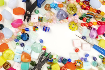 An overhead photo of many different beads with tools for making jewellery, on a white background with a place for text