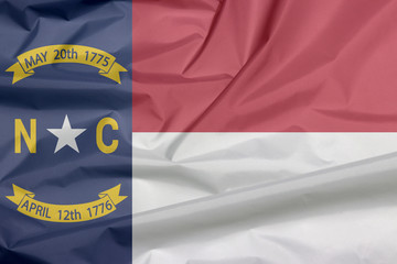 Fototapeta premium Fabric flag of North Carolina. Crease of North Carolina flag background, A blue union, a white star with N and C, the circle containing the same to be one-third.
