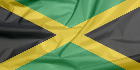 Fabric flag of Jamaica. Crease of Jamaican flag background, A gold diagonal cross divides the field into four triangles of green and black.