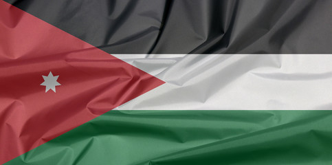 Fabric flag of Jordan. Crease of Jordanian flag background, horizontal triband of black, white and green; with a red chevron and star.