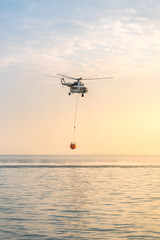 A fire helicopter collects water into the sea and flies toward the mountains to extinguish a forest fire. Rescue operation. Forest Fire Prevention