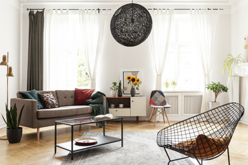 Plant next to couch and sunflowers on cabinet in white flat interior with armchair and lamp. Real...