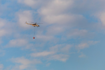 A fire fighter helicopter with a full basket of water flies against a beautiful sky. Rescue operation. Forest Fire Prevention