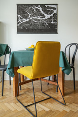 A minimalist city map poster on a white wall of a dining room interior with a yellow chair on herringbone parquet floor