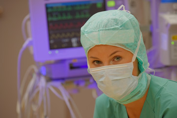 A young woman poses in an operation theater  fully dressed as a anesthetic theater nurse with a face mask and green sterile medical work clothing.