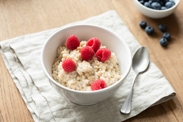 Oatmeal porridge with berry fruits on linen textile. Healthy breakfast food, dieting and healthy eating concept