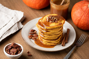 Homemade pumpkin pancakes with cinnamon, caramel and nuts on rustic wooden table