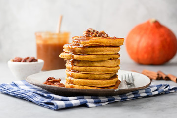 Stack of pumpkin pancakes with caramel sauce and pecan nuts on a plate, closeup view. Tasty autumn...
