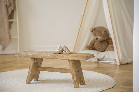 Wooden stool with shoes on white round rug in kid's room interior with plush toy in tent. Real photo