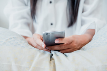Woman hands using smart phone on the bed in the house.