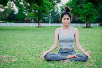 Asian woman practices yoga and meditates on meadow in the park.