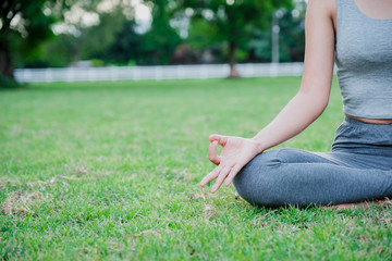 Asian woman practices yoga and meditates on meadow in the park.