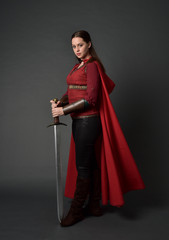  full length portrait of brunette girl wearing red medieval costume and cloak. standing pose ...