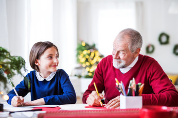 A small girl and her grandfather writing Christmas cards together.