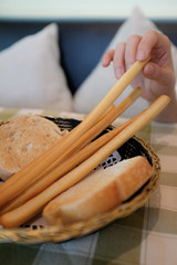 Close up of a person picking up a breadstick from a basket of bread in a restaurant