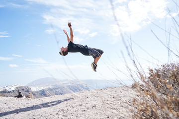 Mann macht Parkour und springt einen Salto vor der K&uuml;ste Santorins 