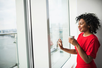 A woman standing by the window holding coffee cup, looking out. Copy space.