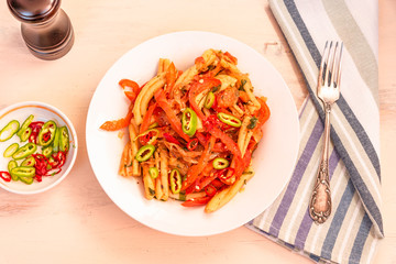 Italian food - Pasta with red pepper and parmesan on a white plate on a rustic light table, top view