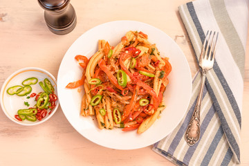 Italian food - Pasta with red pepper and parmesan on a white plate on a rustic light table, top view