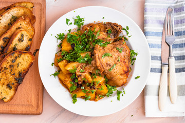 Italian food - stewed chicken with potatoes in tomato sauce on a plate and toasted bread, close-up