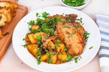 Italian food - stewed chicken with potatoes in tomato sauce on a plate and toasted bread, close-up