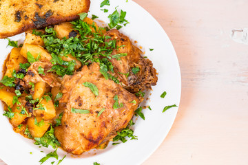 Chicken stew with potatoes in tomato sauce, with parsley on a plate and toasted bread, close-up, copy space for recipe
