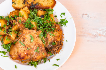 Chicken stew with potatoes in tomato sauce, with parsley on a plate and toasted bread, close-up, copy space for recipe