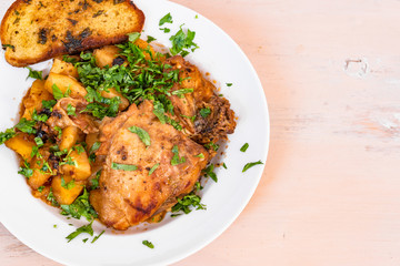 Chicken stew with potatoes in tomato sauce, with parsley on a plate and toasted bread, close-up, copy space for recipe