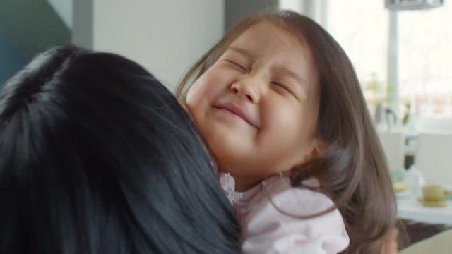 Close up shot of playful little Asian girl hugging her mother