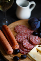 Charcuterie, grilled sausages, cheese, salami, plum olives and a glass of wine on a dark table