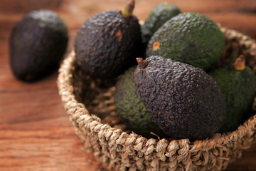 Hass avocado in seagrass basket on rustic wooden table. Healthy fruits concept. Selective focus and free space for text.