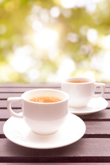 Two cup of hot coffee on wooden table have bokeh in background. 