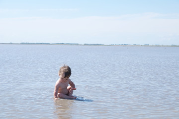 Sitting baby among the lake at summer. Salt shallow lake in Russia. Loneliness  concept in big world