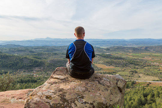 Man sitter p&aring; p&aring; bergstopp och tittar p&aring; utsikten &ouml;ver dalen