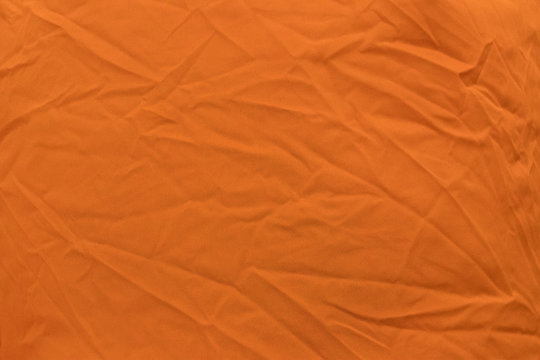 Bright orange fabric with light folds closeup, may be used as background or texture
