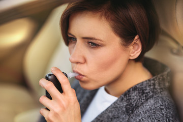 Young millennial woman using breath alcohol analyzer in the car. Closeup with selective focus. Girl taking alcohol test with breathalyzer.