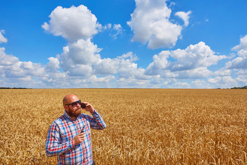 farmer smokes electronic cigarette in a ripe field of wheat with blue sky
