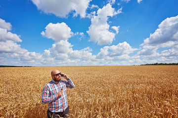 farmer smokes electronic cigarette and call in a ripe field of wheat with blue sky