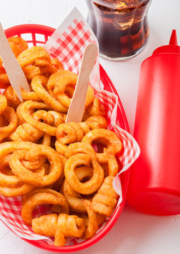 Curly fries fast food snack in red plastic tray with glass of cola and ketchup on stone kitchen background. Unhealthy junk food