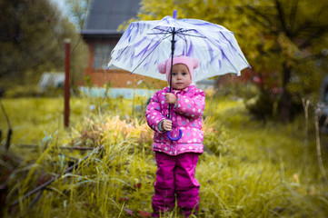 A little girl walks with an umbrella in the rain in the country.