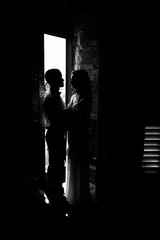 Tender hugs of wedding couple standing before the open door in a dark room